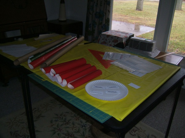 two card tables with gift-wrapping supplies 
                     on top of windbreaker in progress
